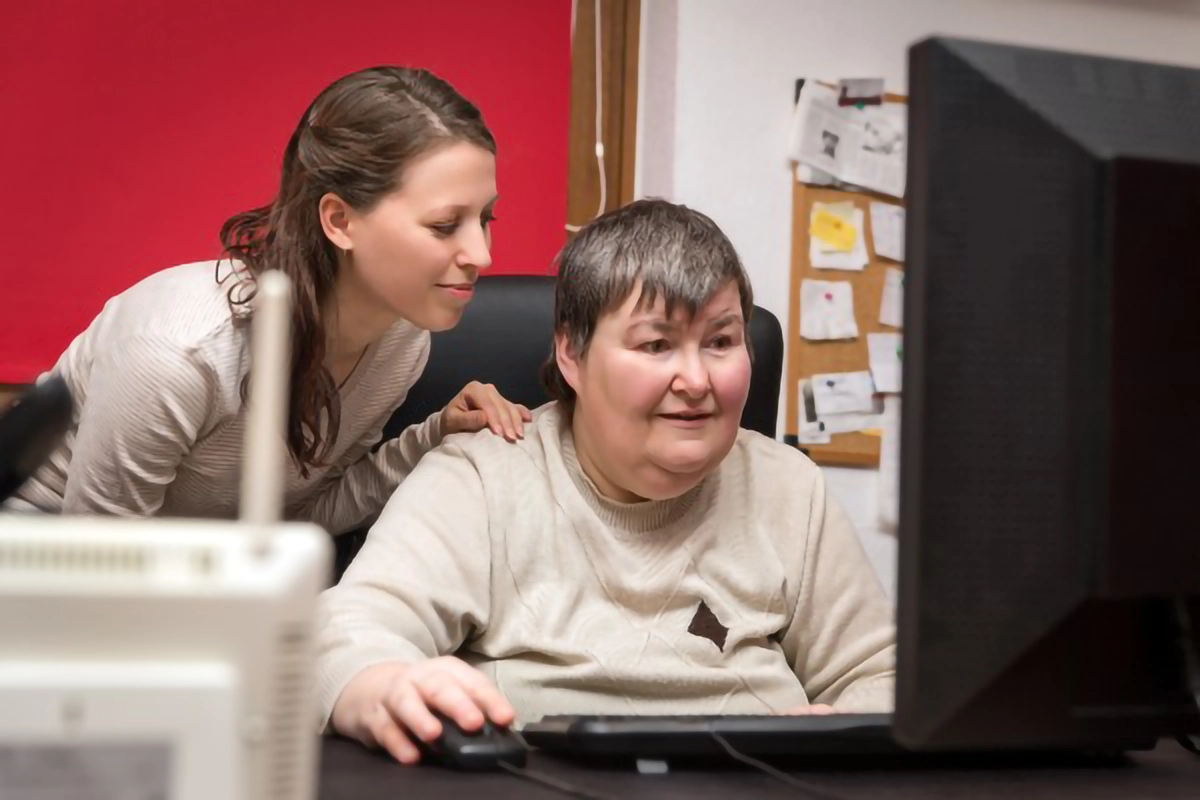 image depicting a patient with learning disabilities being assisted on a computer by a member of staff